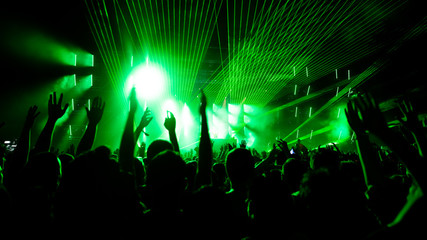 Back view of audience with arms raised in front of stage at music concert.