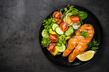 Grilled salmon fish steak with vegetables on black.