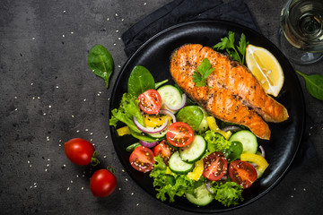 Grilled salmon fish steak with vegetables on black.