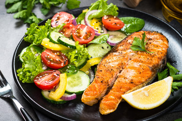 Grilled salmon fish steak with vegetables on black.