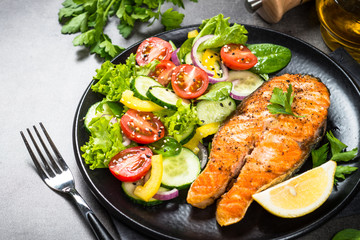 Grilled salmon fish steak with vegetables on black.