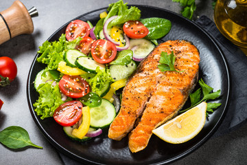 Grilled salmon fish steak with vegetables on black.