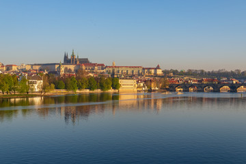 Fototapeta na wymiar Outdoor sunny view of Charles Bridge, Prague Castle, St. Vitus Cathedral and riverside of Vltava River in Prague, Czech Republic in the morning with blue sunrise sky and daybreak atmosphere.