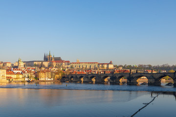 Outdoor sunny view of Charles Bridge, Prague Castle, St. Vitus Cathedral and riverside of Vltava River in Prague, Czech Republic in the morning with blue sunrise sky and daybreak atmosphere.
