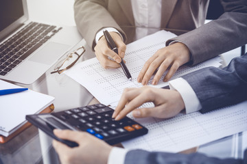 Two female accountants counting on calculator income for tax form completion hands close-up....