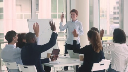 Diverse employees and female coach raise hands at business training