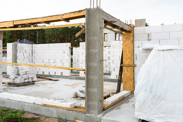 The walls of a house built of white brick with reinforced concrete pillars at the end of which there are ribbed rods, wooden formwork visible from the pillars.