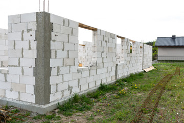 The walls of a house built of white brick with reinforced concrete pillars at the end of which there are ribbed rods, wooden formwork visible from the pillars.