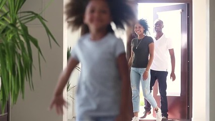 Happy african child girl with parents running into new house