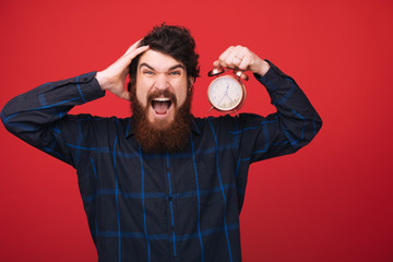 Hate being late. Man hold alarm clock in hand. bearded man with clock over red background