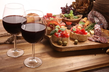 Traditional italian antipasto bruschetta appetizer with cherry tomatoes, cream cheese, basil leaves and balsamic vinegar on cutting board with prosciutto, salami, cheese