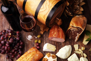 Still life in a rustic style. Grapes on a wooden table with a bottle of wine and meat and cheese. Antipasto and red wine