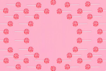 Round frame of lollipops with red and white stripes on a pink background.