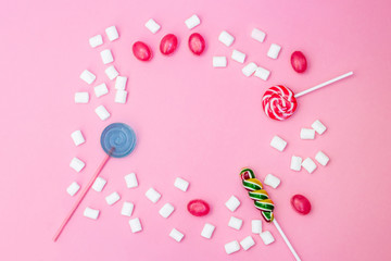 Flat lay composition with frame of lollipops and marshmallows and space for text on pink background.