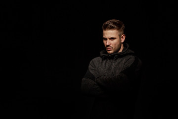 Muscular model young man with beard in hoody on dark background. Fashion portrait of brutal sporty sexy strong muscle guy with modern trendy hairstyle. Model, fashion concept.