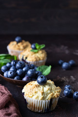 Blueberry muffins with fresh berries and mint leaves on dark brown stone background. Copy space.