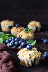 Blueberry muffins with fresh berries and mint leaves on dark brown stone background. Copy space.