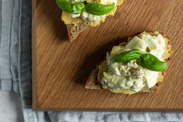 Sandwich with egg salad with avocado and hummus decorated with basil on wooden board and fresh ingredients for making sandwiches. 