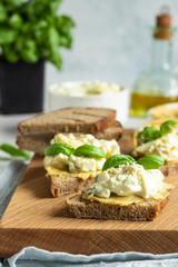 Sandwich with egg salad with avocado and hummus decorated with basil on wooden board and fresh ingredients for making sandwiches. 