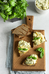 Sandwich with egg salad with avocado and hummus decorated with basil on wooden board and fresh ingredients for making sandwiches. 