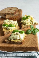 Sandwich with egg salad with avocado and hummus decorated with basil on wooden board and fresh ingredients for making sandwiches. 