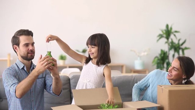Cute kid daughter helping parents unpacking boxes in new home