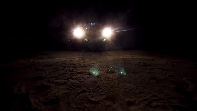 headlights of a car at night, lighting the sand surface in front