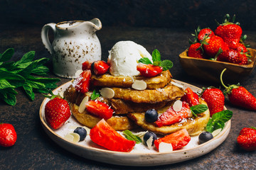 Stecked french toast topped with strawberries, blueberries, mint, ice cream and maple syrup