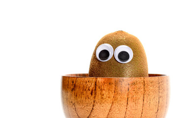 Kiwi fruit with googly toy eyes sitting in the bamboo bowl isolated on white background.