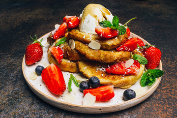 Stecked french toast topped with strawberries, blueberries, mint, ice cream and maple syrup