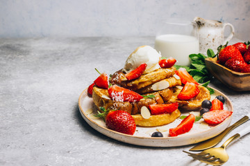 Stecked french toast topped with strawberries, blueberries, mint, ice cream and maple syrup
