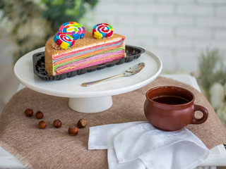 rainbow cake on a stand and a Cup of tea on a light background