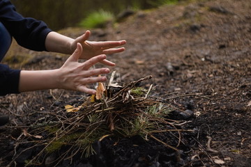 Open palms of a child folding a fire from dry branches and leaves