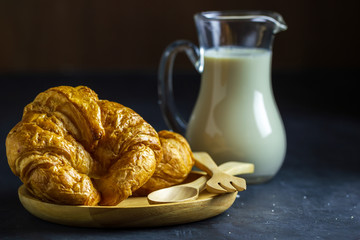 Croissants on wooden dish and milk jug on table in dark background.