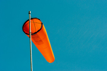 Downward angled plain orange windsock against a clear blue sky.