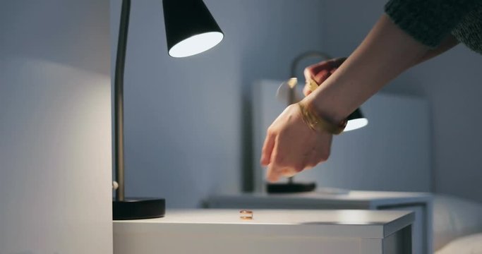 Business woman taking off her watch and putting it on the nightstand with her ring before going to bed in hotel bedroom. Young entrepreneur on business trip.