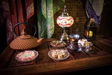 Arabian tea in glass with eastern snacks on vintage wooden surface. Eastern tea concept. Low light lounge interior with carpet. Empty space.