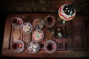 Arabian tea in glass with eastern snacks on vintage wooden surface. Eastern tea concept. Low light lounge interior with carpet. Empty space.