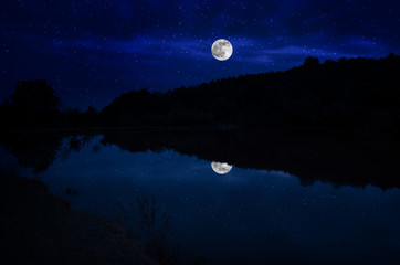 Naklejka na ściany i meble This dramatic moon rise in a deep blue night time sky is accented by highlighted clouds and beautiful, calm lake reflection.Selective focus
