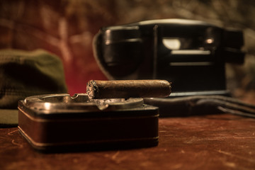 Close up of a Cuban cigar and ashtray on the wooden table. Communist dictator commander table in dark room. Army general`s work table concept.