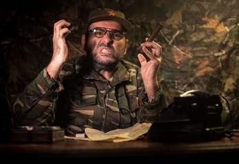 The evil dictator sitting on table. Angry communist general sitting at headquarter or Cuban commander in dark room.