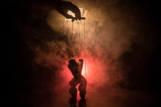 Concept of manipulation. Hand holds strings for manipulation. The hand controls the puppet strings on a dark foggy background.