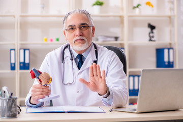 Aged male doctor cardiologist with heart model 