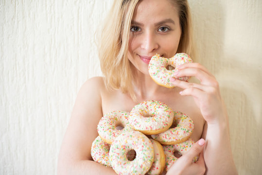 Nude young woman eating donuts. Portrait of an attractive woman with a mountain of donuts
