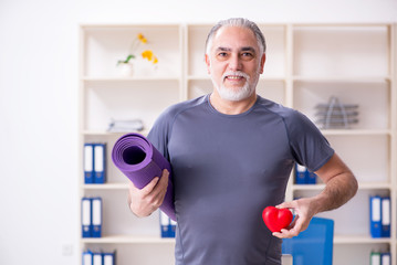 White bearded old man employee doing exercises in the office 