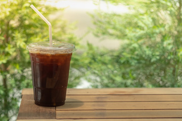 Close up of take away plastic cup of iced black coffee (Americano) under sunlight on wooden table...