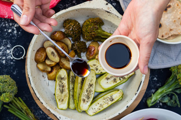 Baked, roasted vegetables on frying pan skillet. Potato, zucchini, potato with spices. Woman hands...