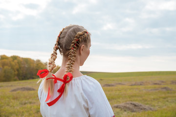 Russian girl Slavic appearance with braids with red ribbons in the field in autumn