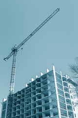 Fototapeta na wymiar tower crane near apartment building under construction against blue sky background