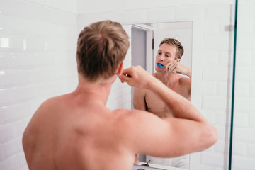 topless muscle man brushing his teeth front of mirror in the bathroom